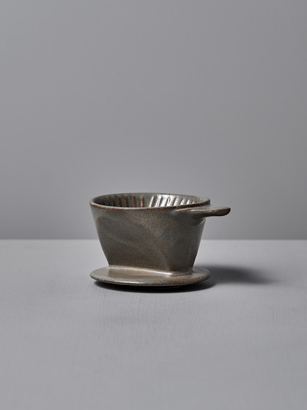 A Mino-yaki Coffee Dripper (2 Cup) – Grey from CHIPS Inc. rests on a flat surface, highlighting its traditional craftsmanship with a handle.