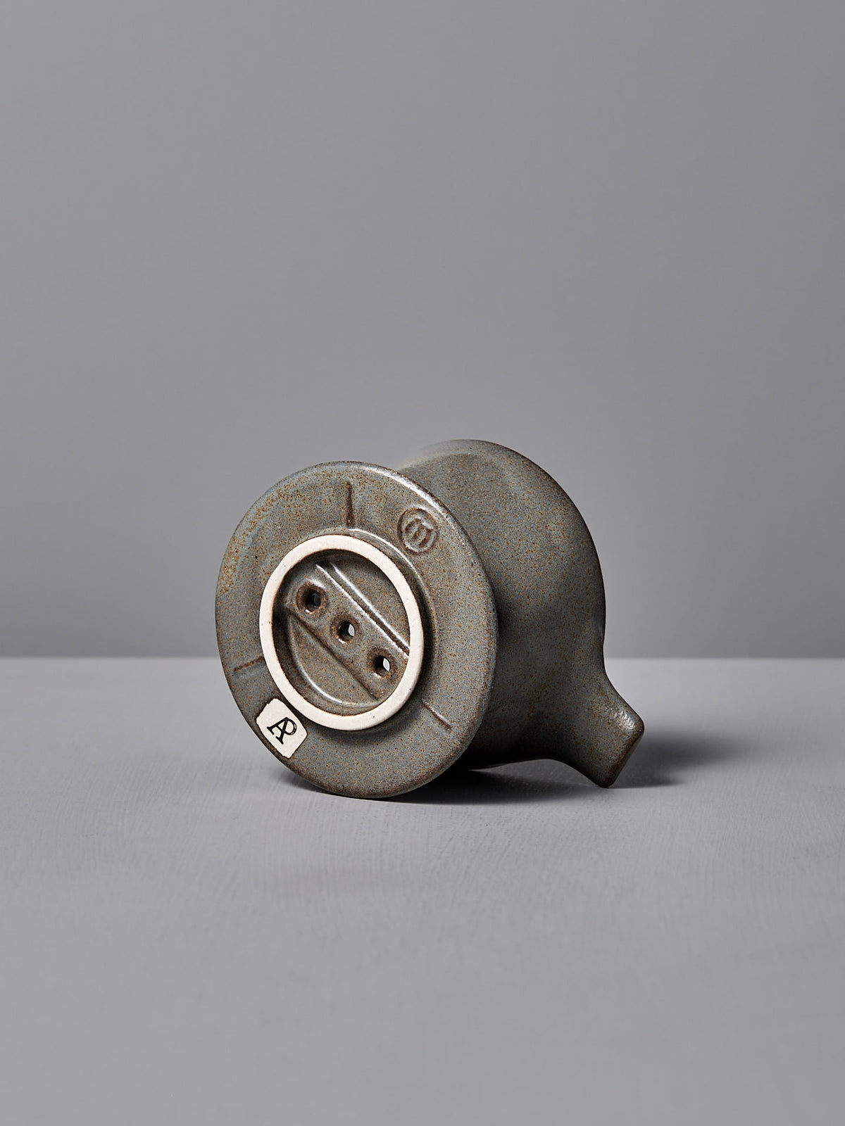 A Mino-yaki Coffee Dripper from CHIPS Inc., resembling a vintage light socket, lies on its side against a gray backdrop, showcasing timeless elegance.