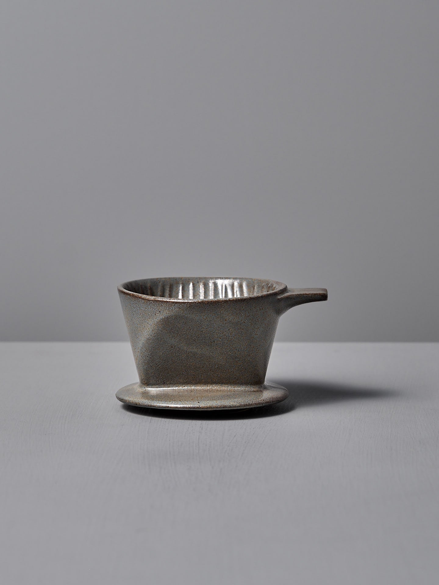 The CHIPS Inc. Mino-yaki Coffee Dripper (2 Cup) – Grey, with its sleek handle design, gracefully sits on a flat surface against a neutral backdrop.