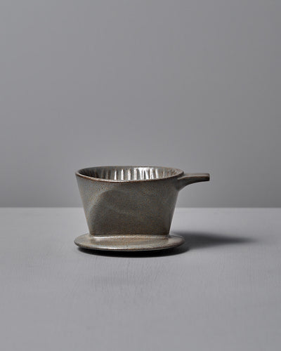 The CHIPS Inc. Mino-yaki Coffee Dripper (2 Cup) – Grey, with its sleek handle design, gracefully sits on a flat surface against a neutral backdrop.