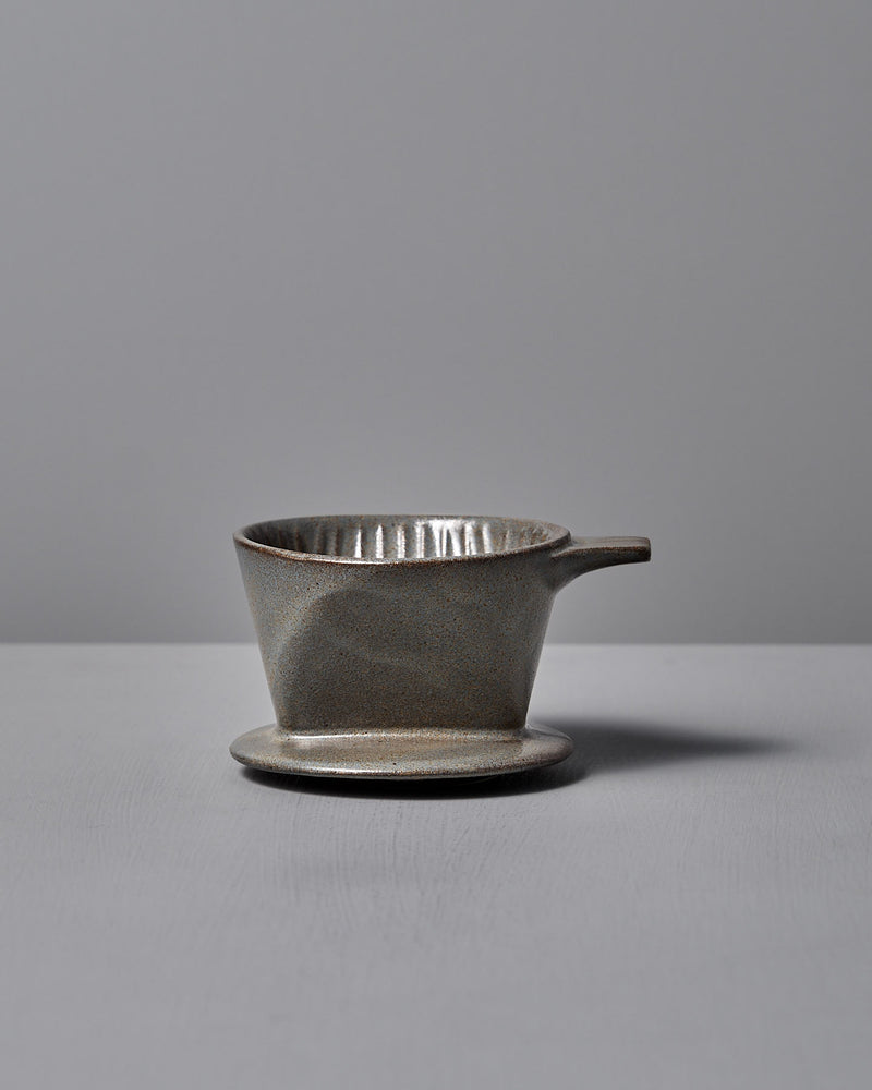 The CHIPS Inc. Mino-yaki Coffee Dripper (2 Cup) – Grey, with its sleek handle design, gracefully sits on a flat surface against a neutral backdrop.