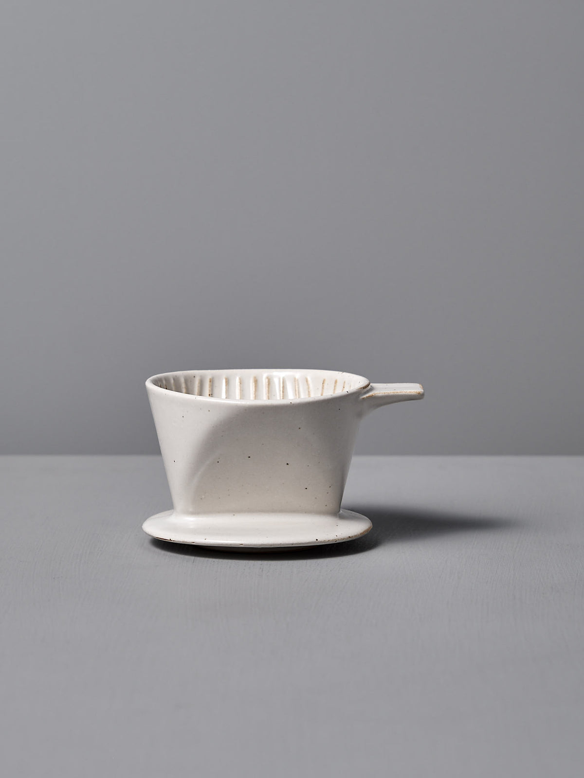 The Mino-yaki Coffee Dripper (2 Cup) – White by CHIPS Inc. is elegantly poised on a flat gray surface against a soft gray background.