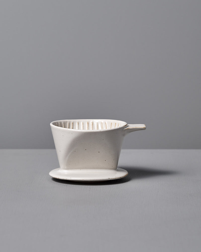 The Mino-yaki Coffee Dripper (2 Cup) – White by CHIPS Inc. is elegantly poised on a flat gray surface against a soft gray background.