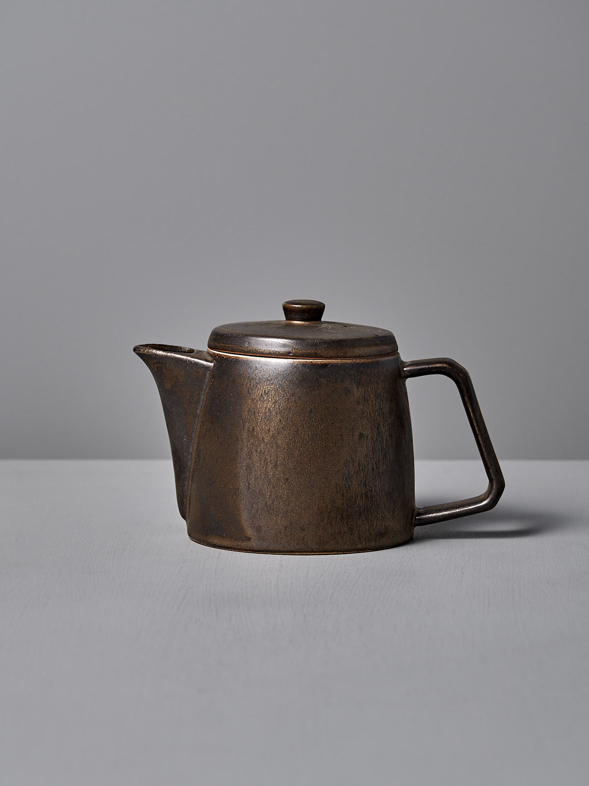 The Mino-yaki Teapot (2 Cup) – Brass by CHIPS Inc. is a brown ceramic teapot with a lid and side handle, ideal for brewing loose leaf tea, elegantly resting on a gray surface.