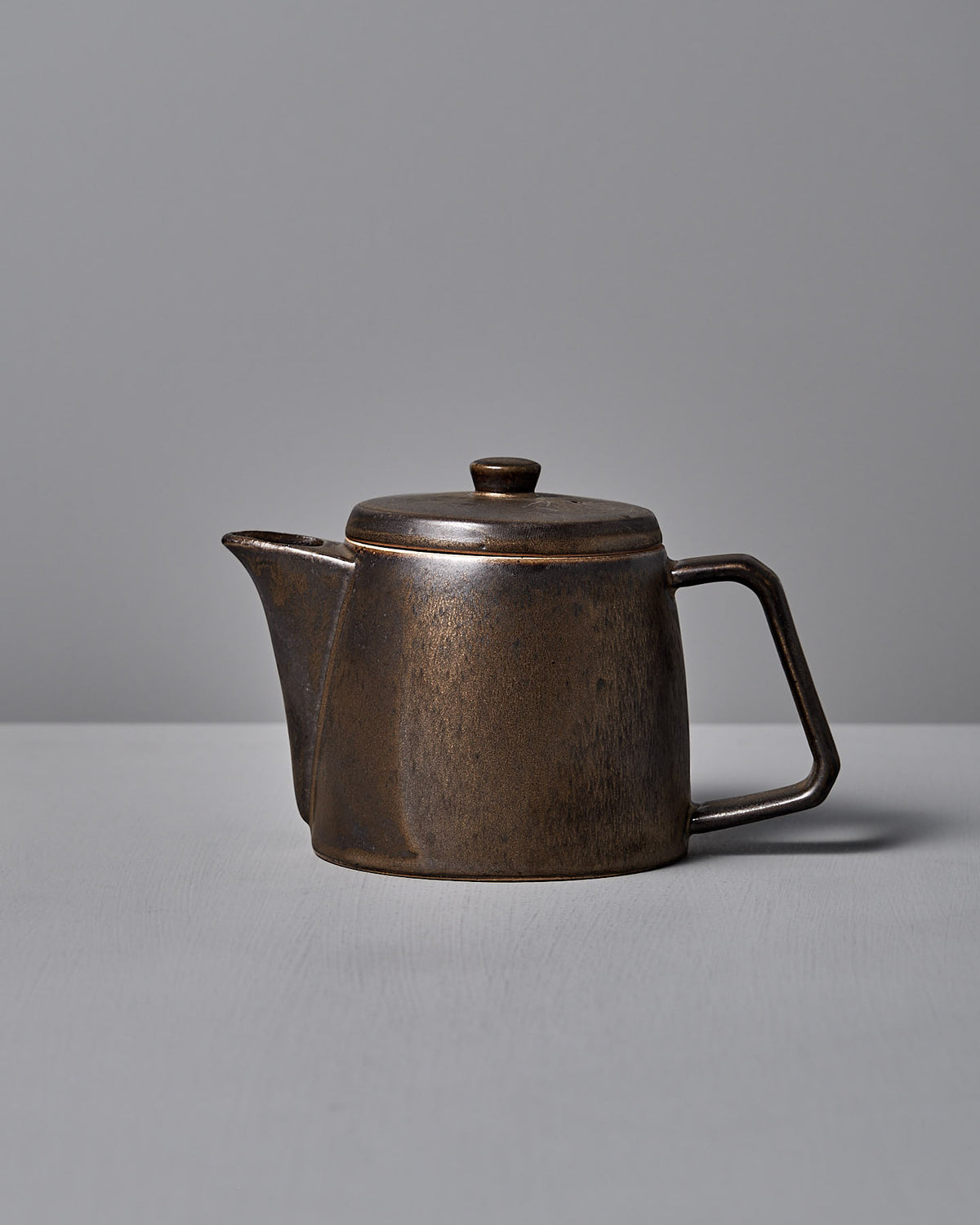 The Mino-yaki Teapot (2 Cup) – Brass by CHIPS Inc. is a brown ceramic teapot with a lid and side handle, ideal for brewing loose leaf tea, elegantly resting on a gray surface.