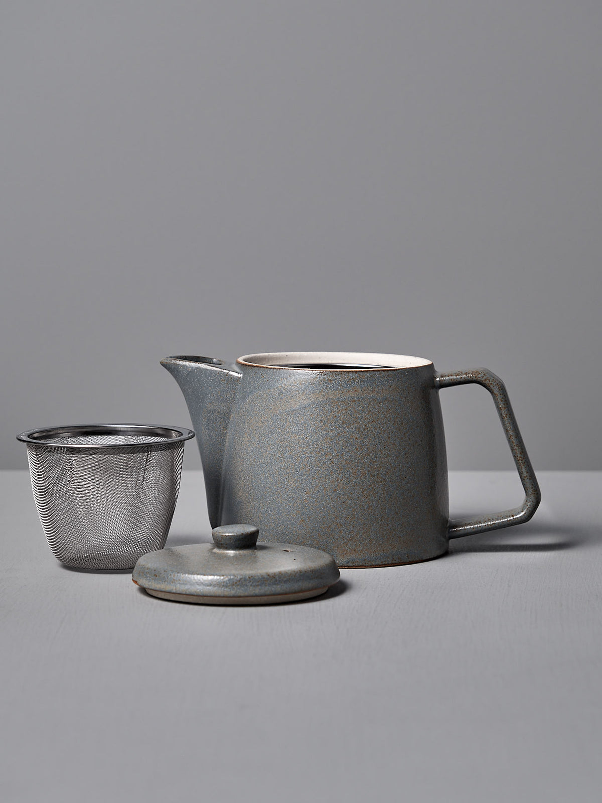 The CHIPS Inc. Mino-yaki Teapot (2 Cup) – Grey, crafted with the Mino-yaki technique, includes a ceramic body and separate lid with a metal strainer against a plain gray backdrop.