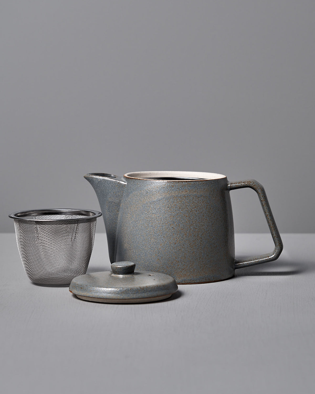 The CHIPS Inc. Mino-yaki Teapot (2 Cup) – Grey, crafted with the Mino-yaki technique, includes a ceramic body and separate lid with a metal strainer against a plain gray backdrop.