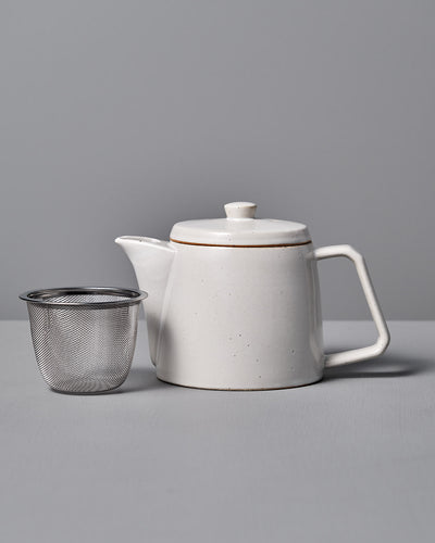 The CHIPS Inc. Mino-yaki Teapot (2 Cup) in white gracefully sits beside a metal infuser on a gray surface, ideal for savoring loose leaf tea.