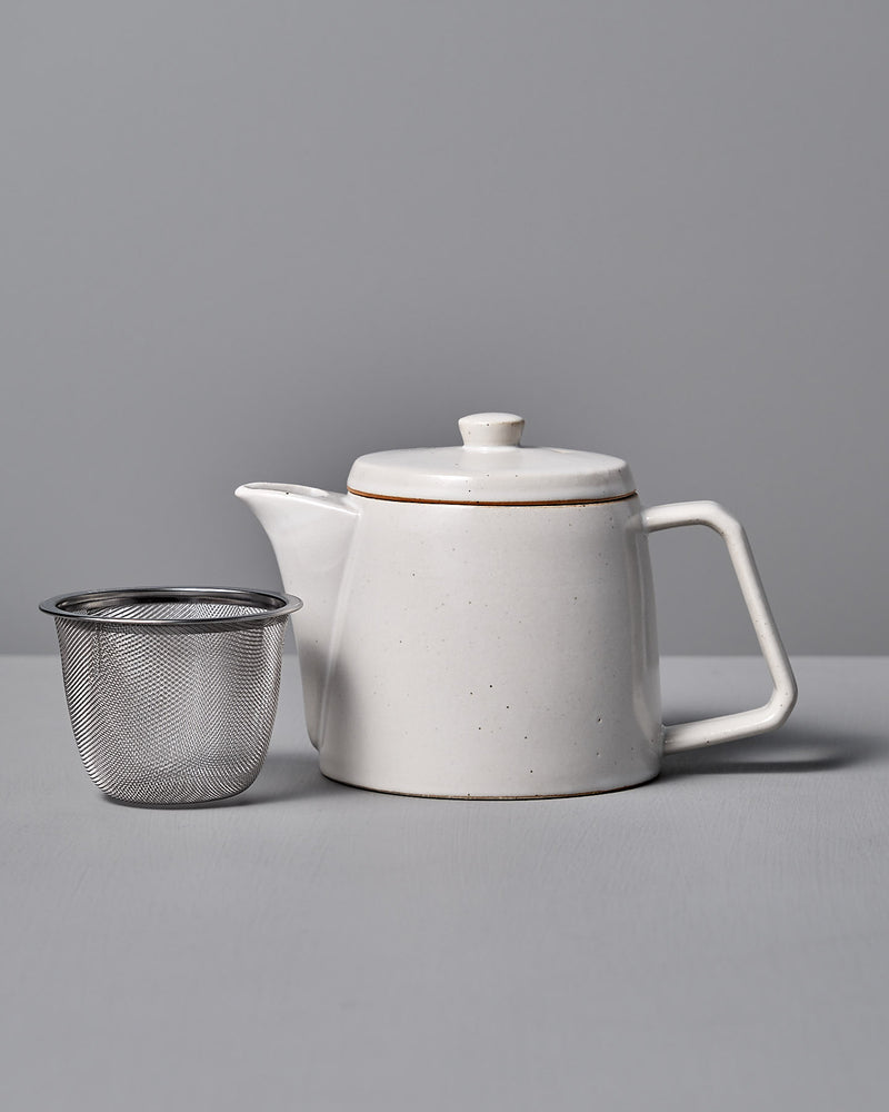 The CHIPS Inc. Mino-yaki Teapot (2 Cup) in white gracefully sits beside a metal infuser on a gray surface, ideal for savoring loose leaf tea.