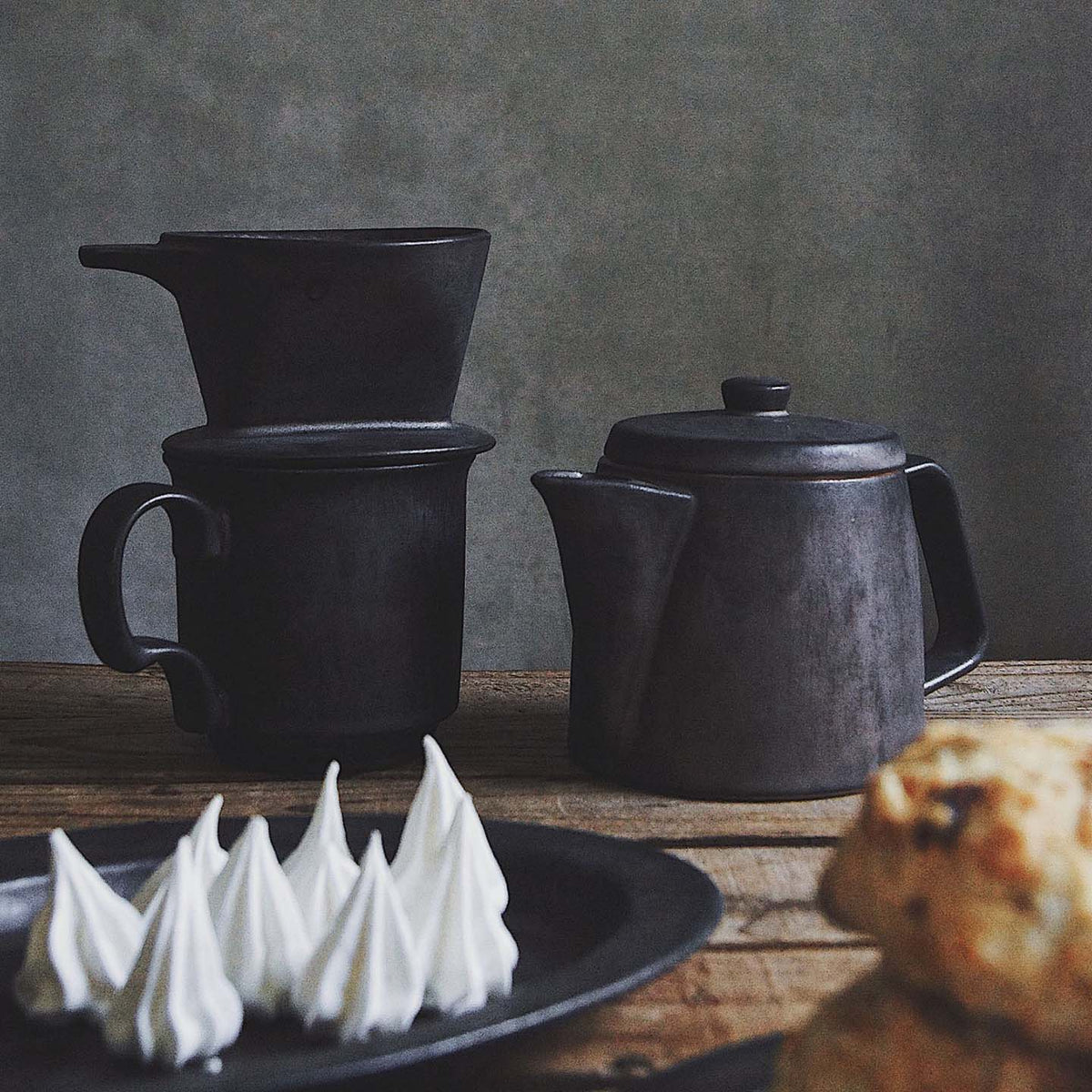 Mino-yaki coffee dripper, crafted in the traditional Mino-yaki style by CHIPS Inc., includes a teapot, two stacked mugs, and a brass coffee dripper on a wooden surface. Nearby are meringue cookies and a scone elegantly placed on a dark plate.