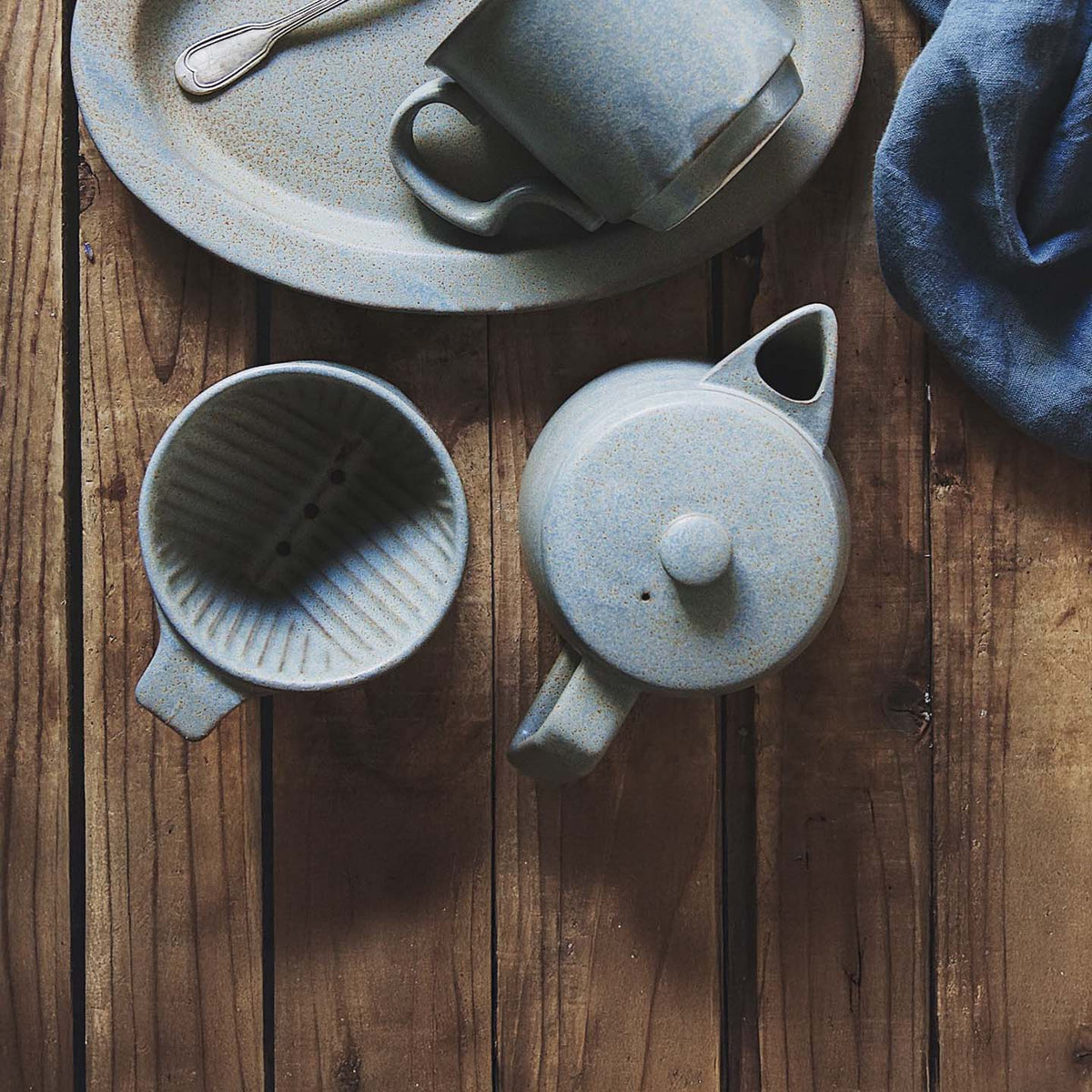 A beautifully crafted Mino-yaki coffee dripper from CHIPS Inc. rests on a wooden table, accompanied by a delicate cloth. This piece showcases the elegance of the ancient pottery traditions reminiscent of the Mino-yaki technique.