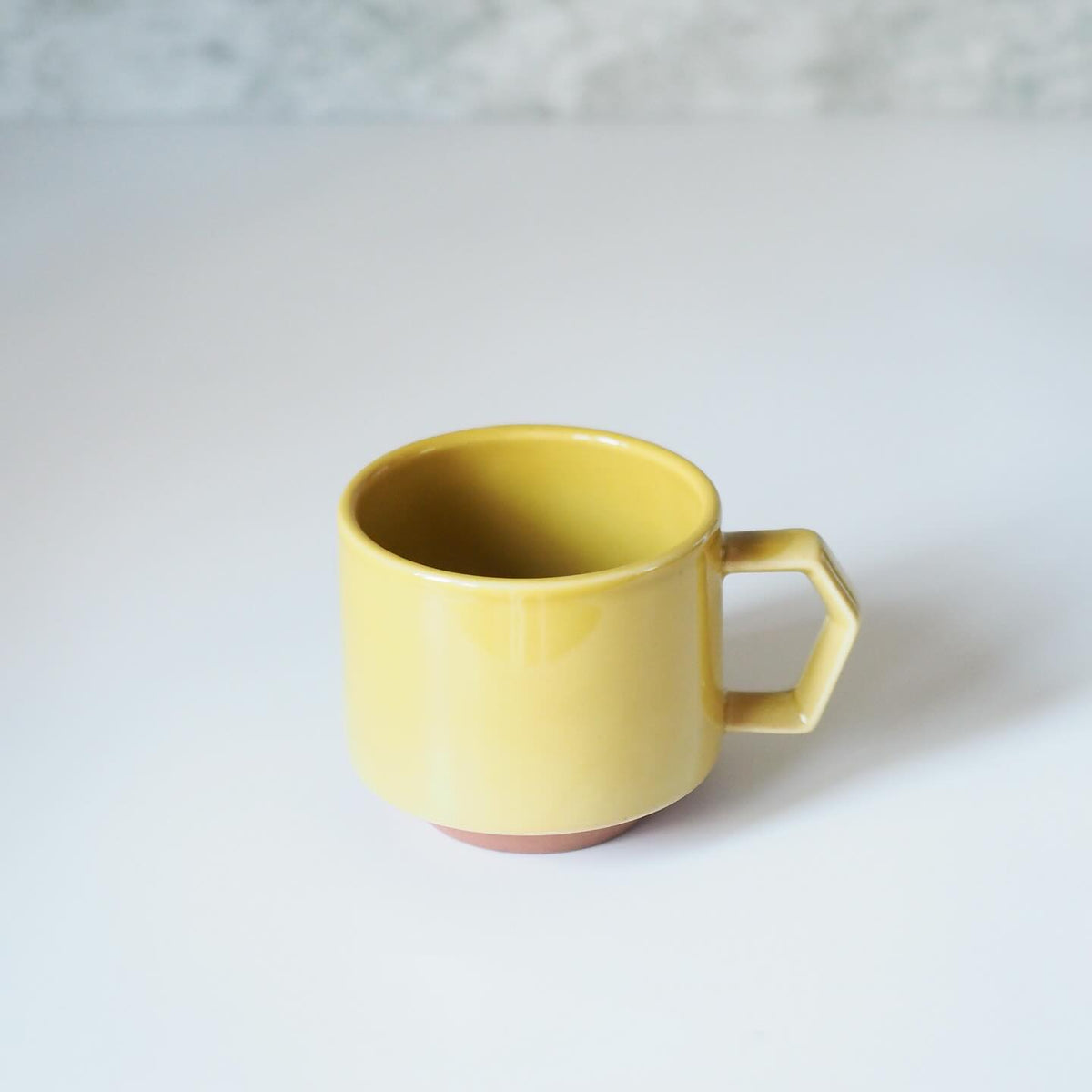 The Stacking Mug – Mustard by CHIPS Inc. sits elegantly on a white surface.