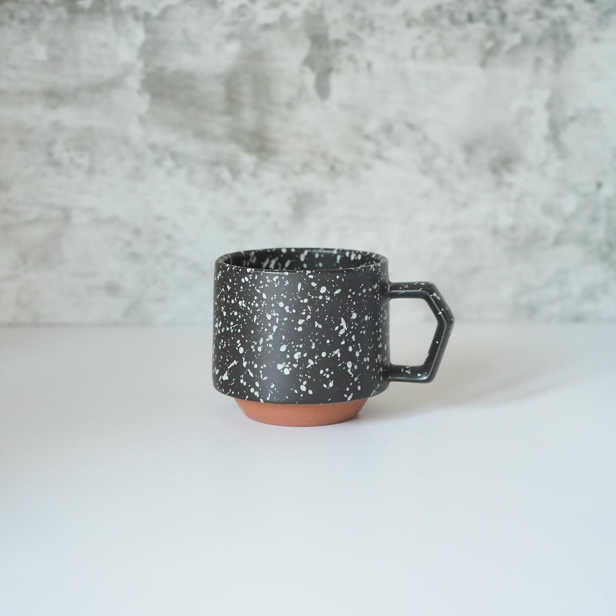 A Stacking Mug – Speckled Black, with a black and white speckled pattern, placed on a table. (Brand: CHIPS Inc.)