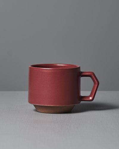 The Stacking Mug – Matte Red by CHIPS Inc., styled with a sleek angular handle and reminiscent of elegant Minoyaki porcelain, sits gracefully on a gray surface.