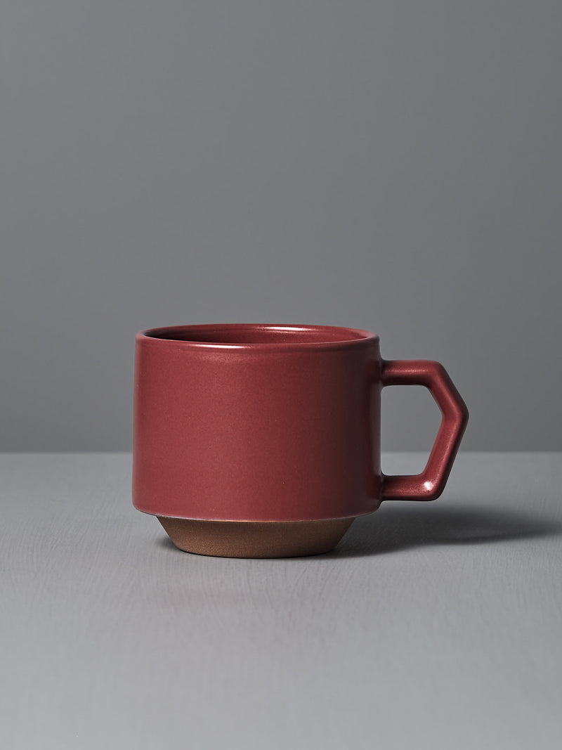 The Stacking Mug – Matte Red by CHIPS Inc., styled with a sleek angular handle and reminiscent of elegant Minoyaki porcelain, sits gracefully on a gray surface.