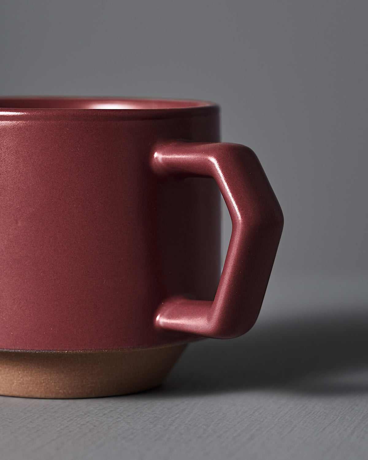 A close-up of the Stacking Mug – Matte Red by CHIPS Inc., crafted from Minoyaki porcelain with a hexagonal handle, is elegantly placed on a gray surface.
