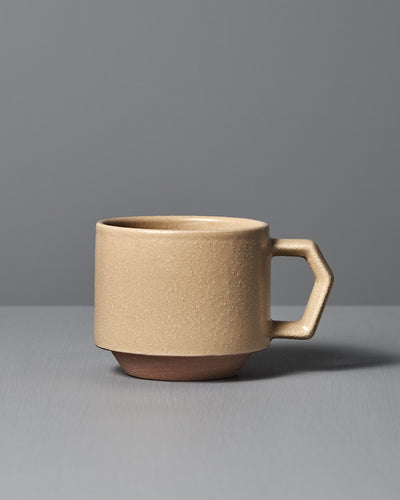 A CHIPS Inc. Stacking Mug – Sand Tan sits on a gray surface against a gray background, highlighting the elegance of Japanese porcelain with its geometric handle.