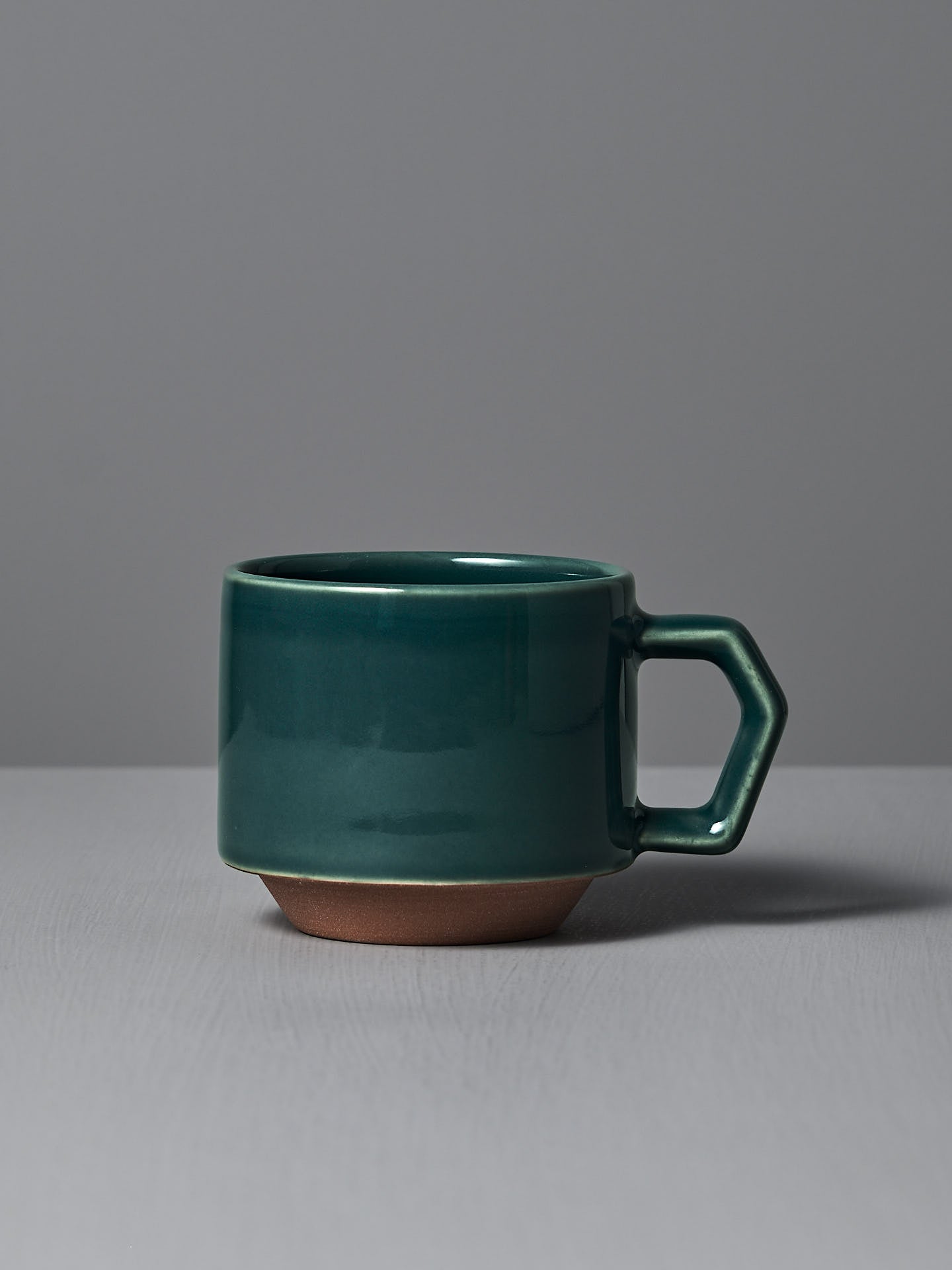The Stacking Mug – Teal by CHIPS Inc., featuring a hexagonal handle, sits elegantly on a gray surface against a gray background.