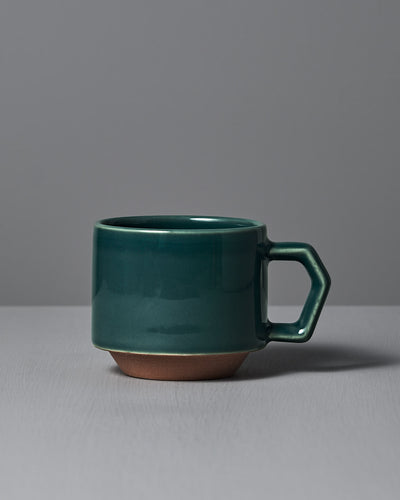 The Stacking Mug – Teal by CHIPS Inc., featuring a hexagonal handle, sits elegantly on a gray surface against a gray background.