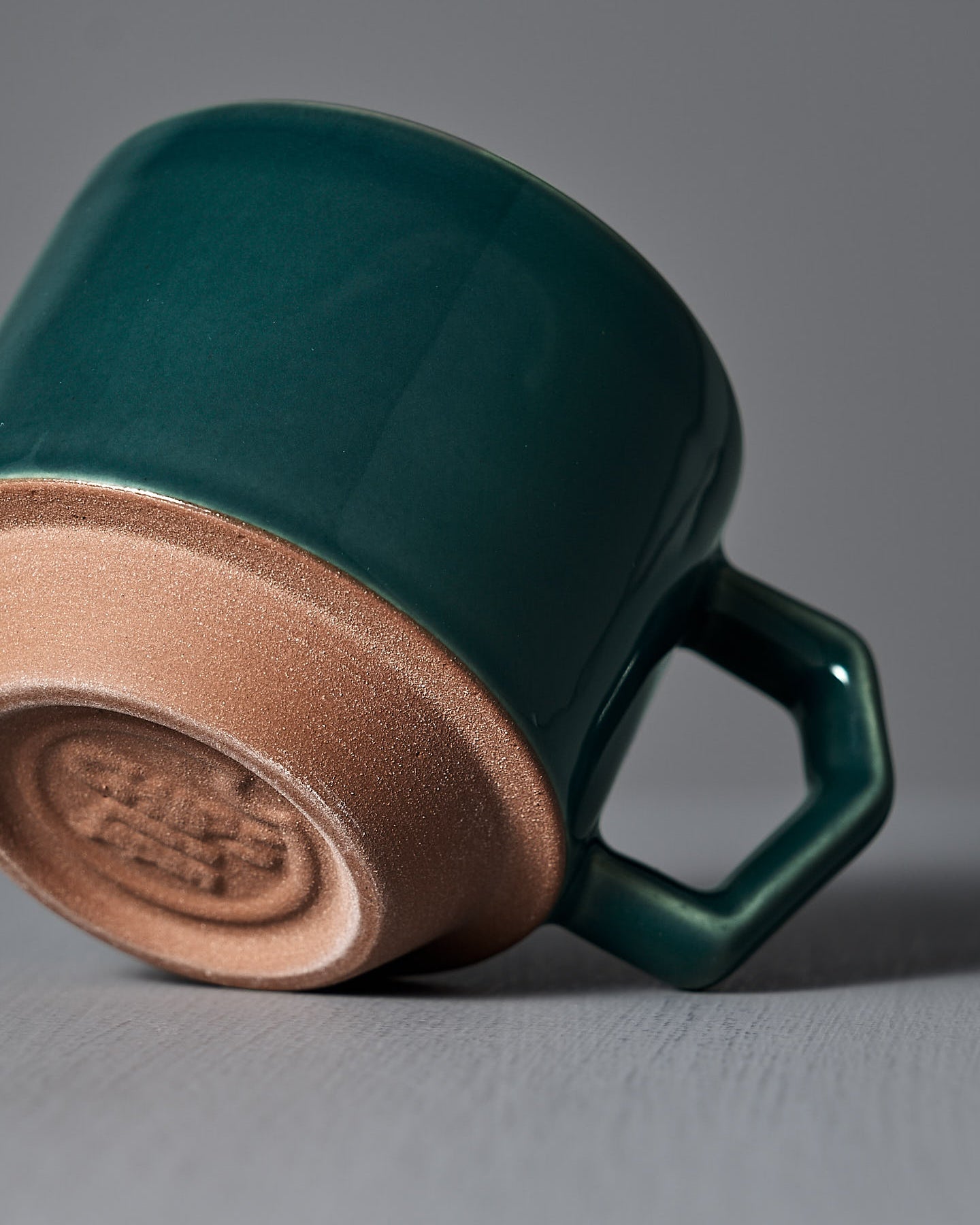 The Stacking Mug – Teal by CHIPS Inc., featuring a hexagonal handle, sits elegantly on a gray surface against a gray background.