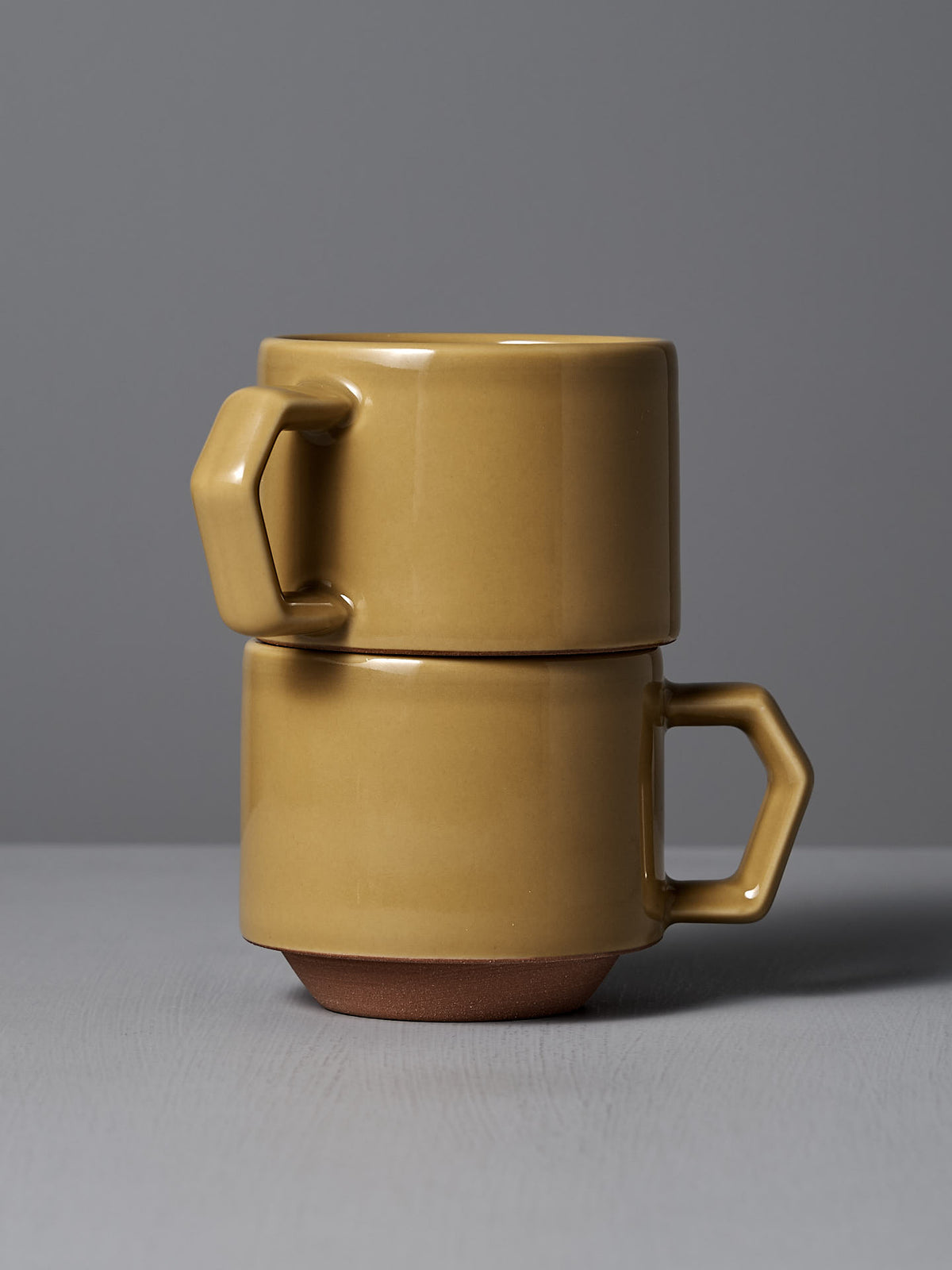 Two stacked Stacking Mugs – Mustard by CHIPS Inc., featuring angular handles, set against a gray background.