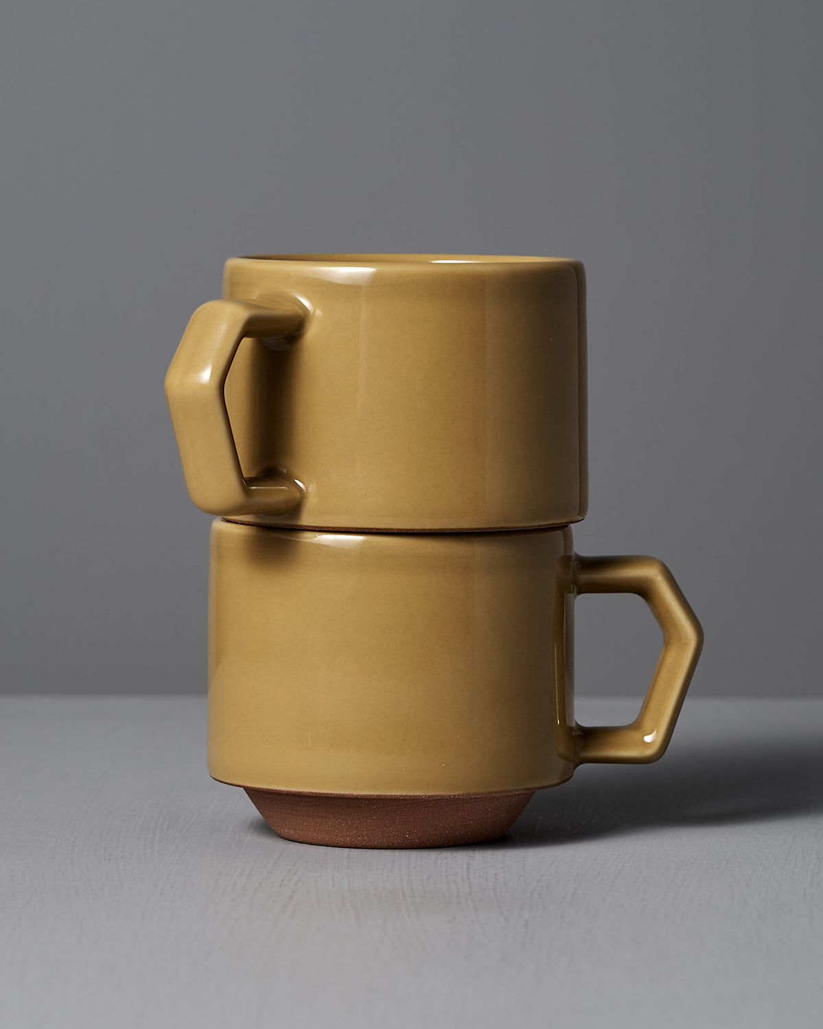 Two stacked Stacking Mugs – Mustard by CHIPS Inc., featuring angular handles, set against a gray background.