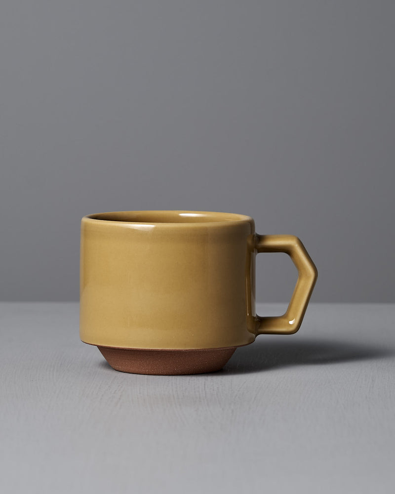 The Stacking Mug – Mustard by CHIPS Inc. exudes elegance as it rests gracefully on a gray surface against a gray background, its geometric handle and matte finish reflecting the refined charm of Minoyaki porcelain.
