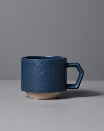 The CHIPS Inc. Stacking Mug – Sand Blue, featuring a geometric handle, rests on a light gray surface, showcasing its handmade porcelain elegance.