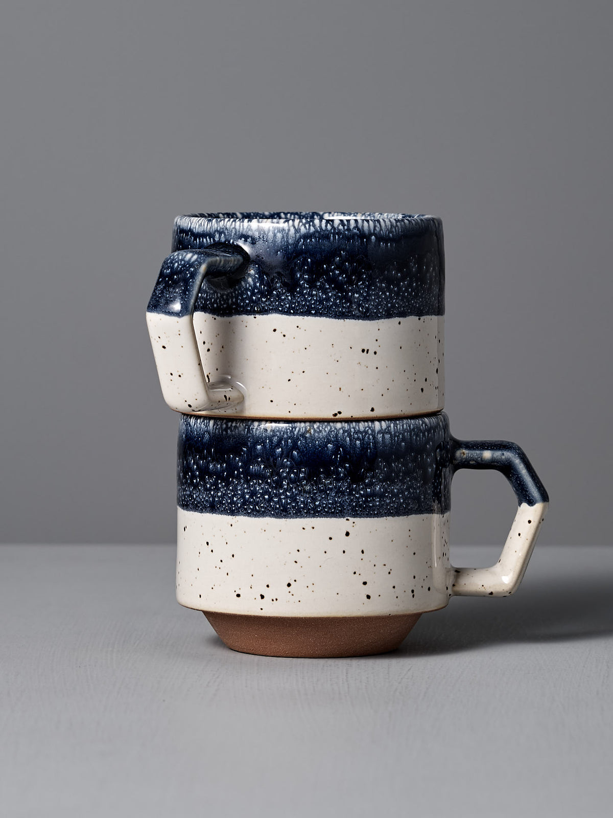 Two Stacking Mugs from CHIPS Inc., featuring a speckled navy and white design with angular handles, are crafted from Minoyaki porcelain and set against a neutral background.