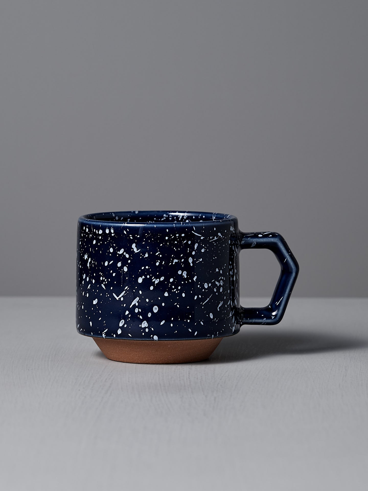 A Stacking Mug in speckled navy by CHIPS Inc. features a hexagonal handle and sits elegantly on a light gray surface, highlighting its stackable design.