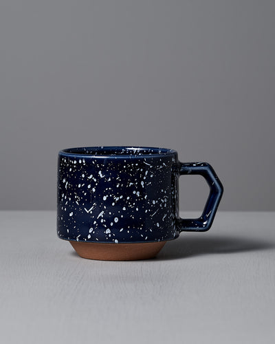 A Stacking Mug in speckled navy by CHIPS Inc. features a hexagonal handle and sits elegantly on a light gray surface, highlighting its stackable design.