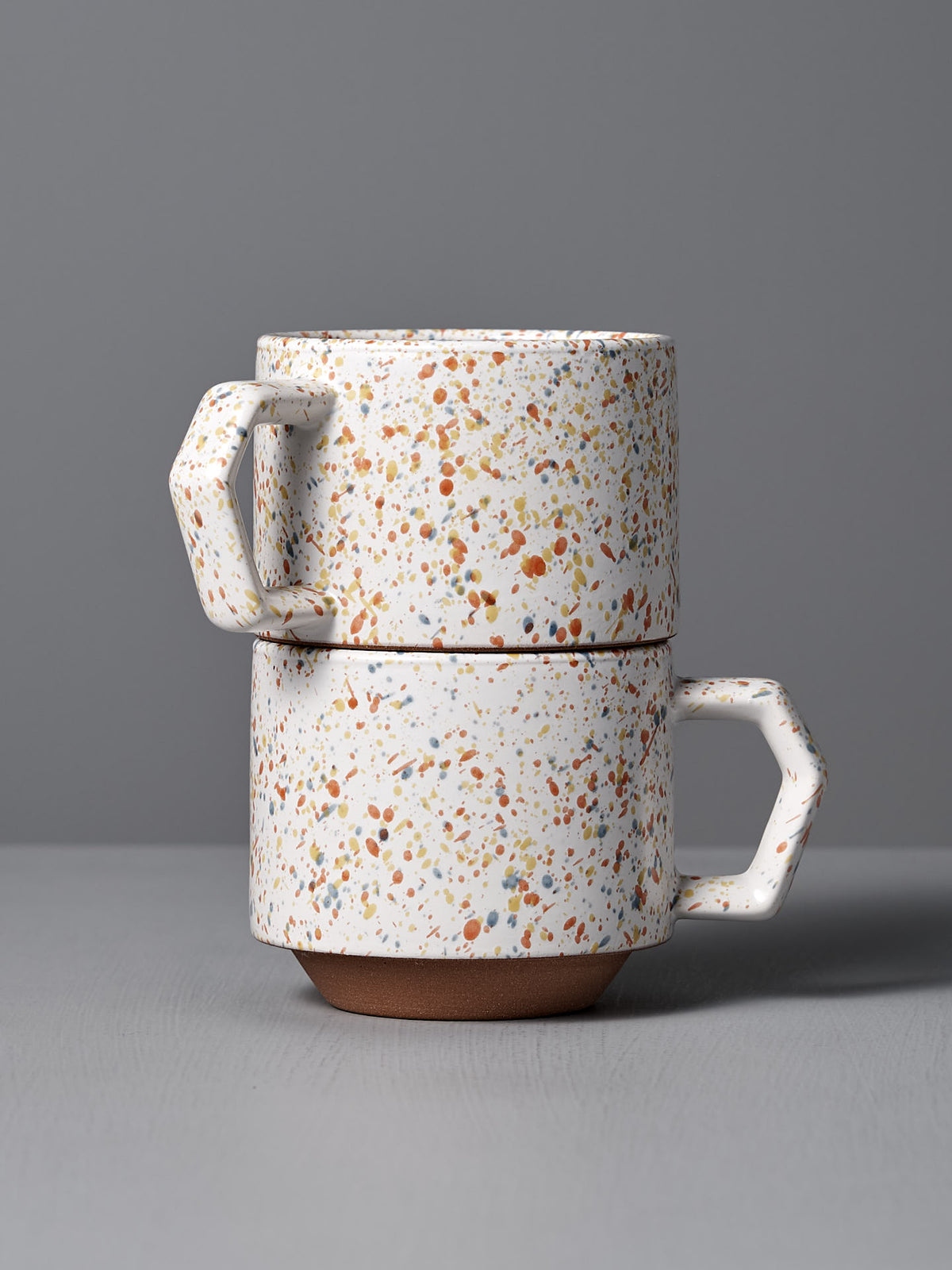 A pair of Stacking Mug – Speckled White by CHIPS Inc., inspired by sophisticated Japanese tableware, is beautifully set against a gray background.