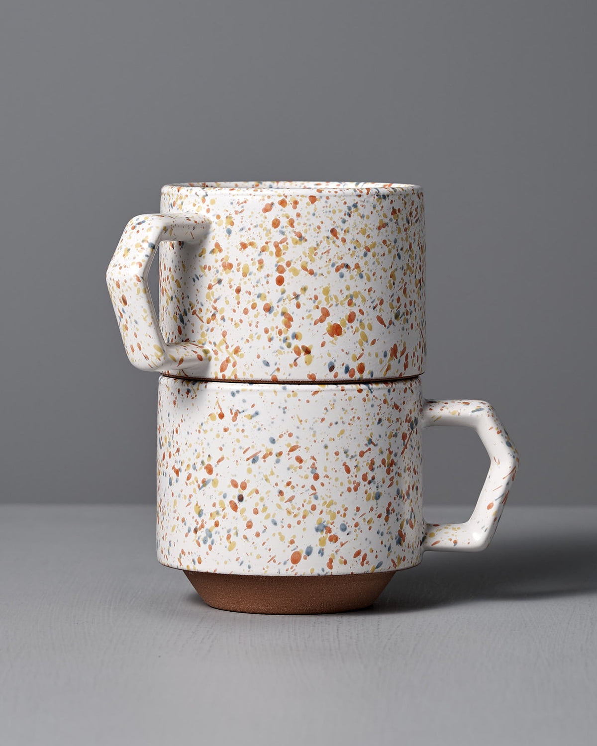 A pair of Stacking Mug – Speckled White by CHIPS Inc., inspired by sophisticated Japanese tableware, is beautifully set against a gray background.