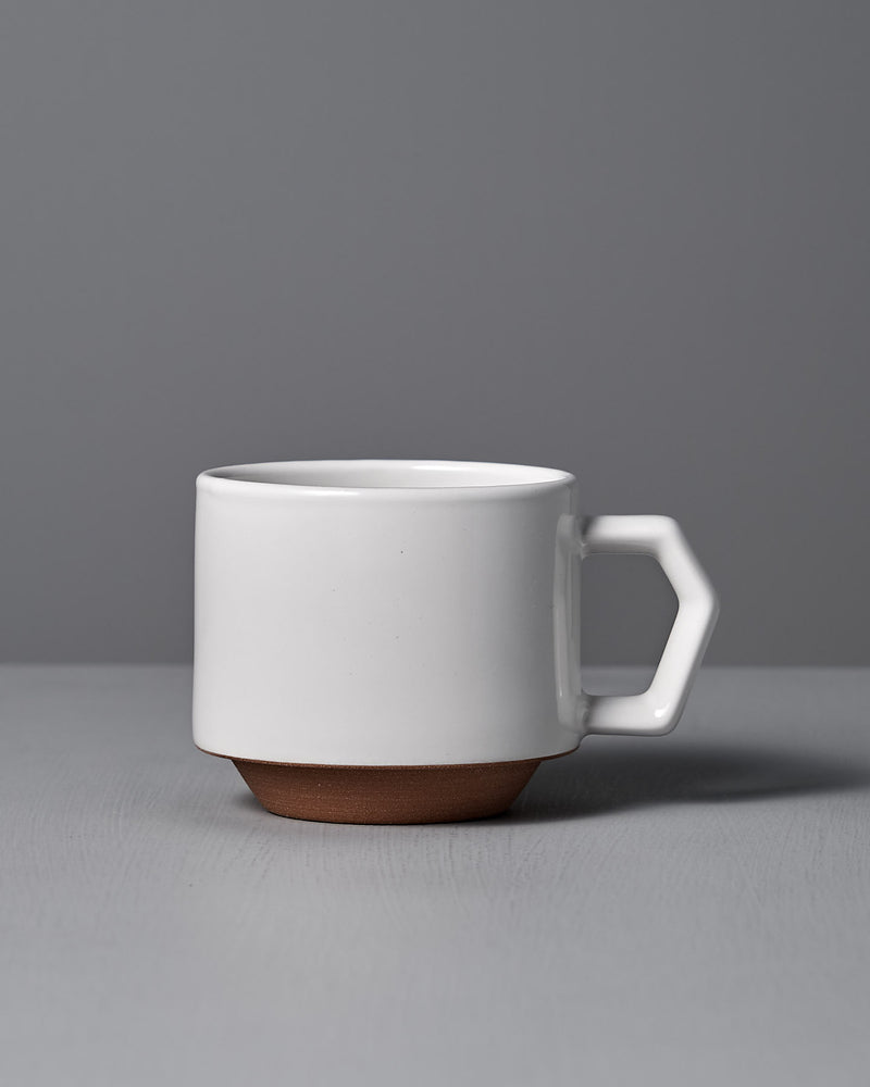 A CHIPS Inc. Stacking Mug – White, featuring a geometric handle and a brown base, sits elegantly on a gray surface against a gray background.