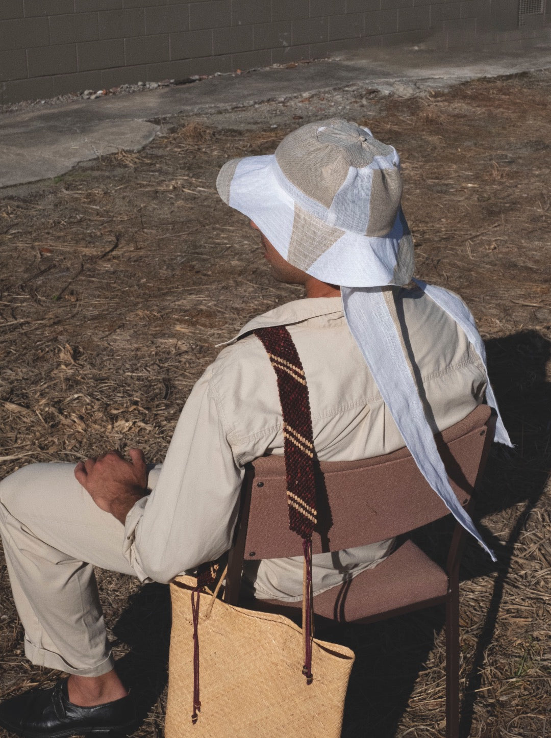 A man sitting on a chair wearing a Companion Classic Brim with Wide Ties – Bold Stripe hat made from 100% recycled textiles.