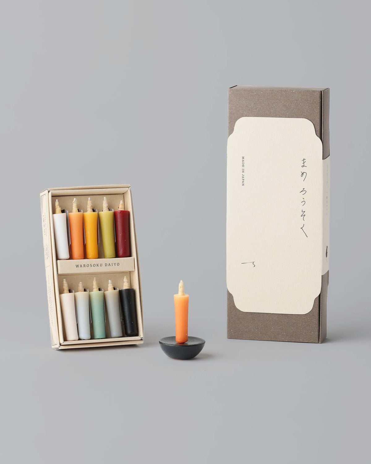 The Daiyo Rice Wax Candle & Ceramic Stand Set – Earth | Black includes a vibrant orange rice wax candle housed in an elegant black holder, accompanied by both open and closed packaging. It's an ideal addition for enhancing your meditation space.