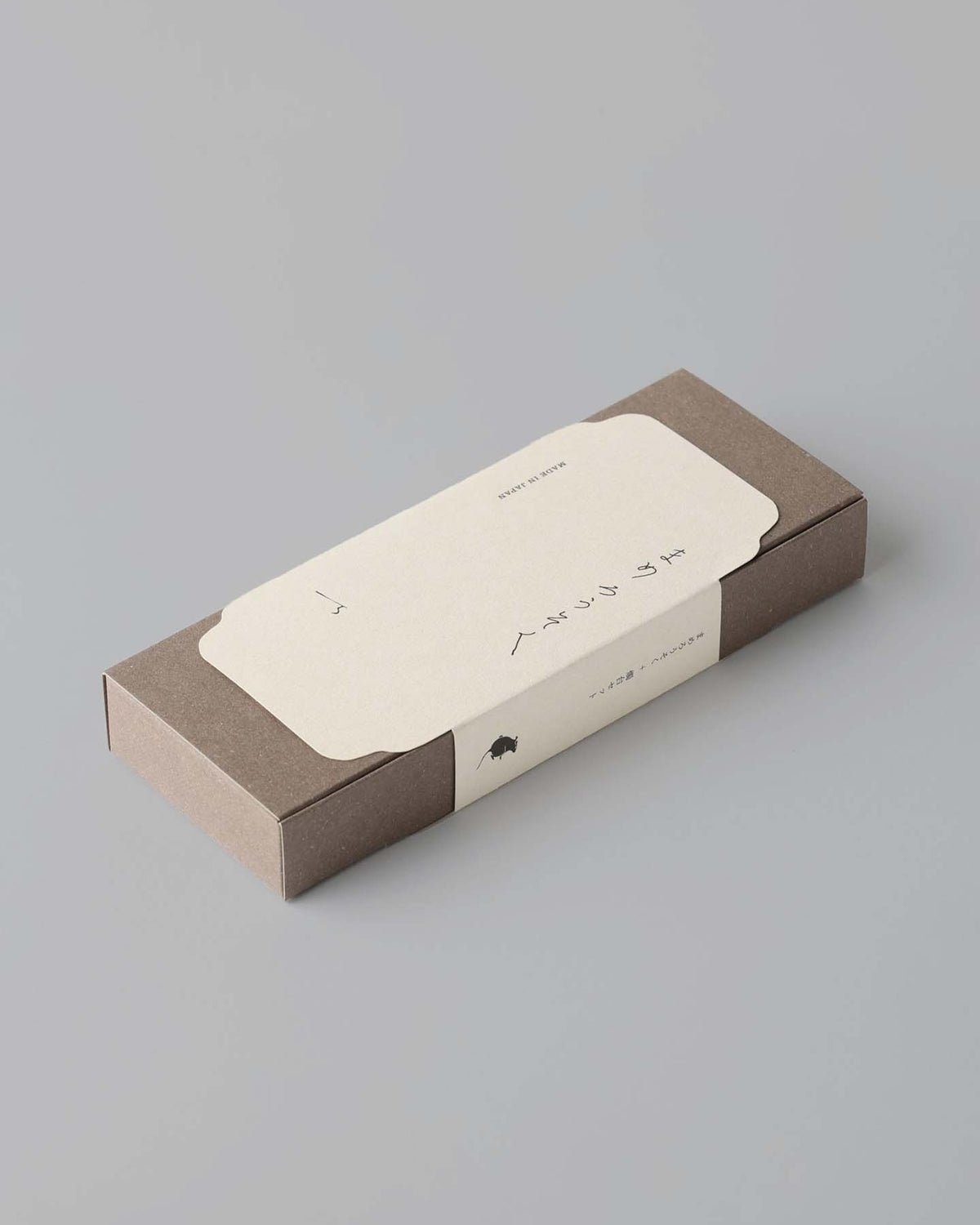A rectangular brown box featuring a beige label with Japanese text and a small black icon encases the exquisite Rice Wax Candle & Ceramic Stand Set – Earth | Black by Daiyo.