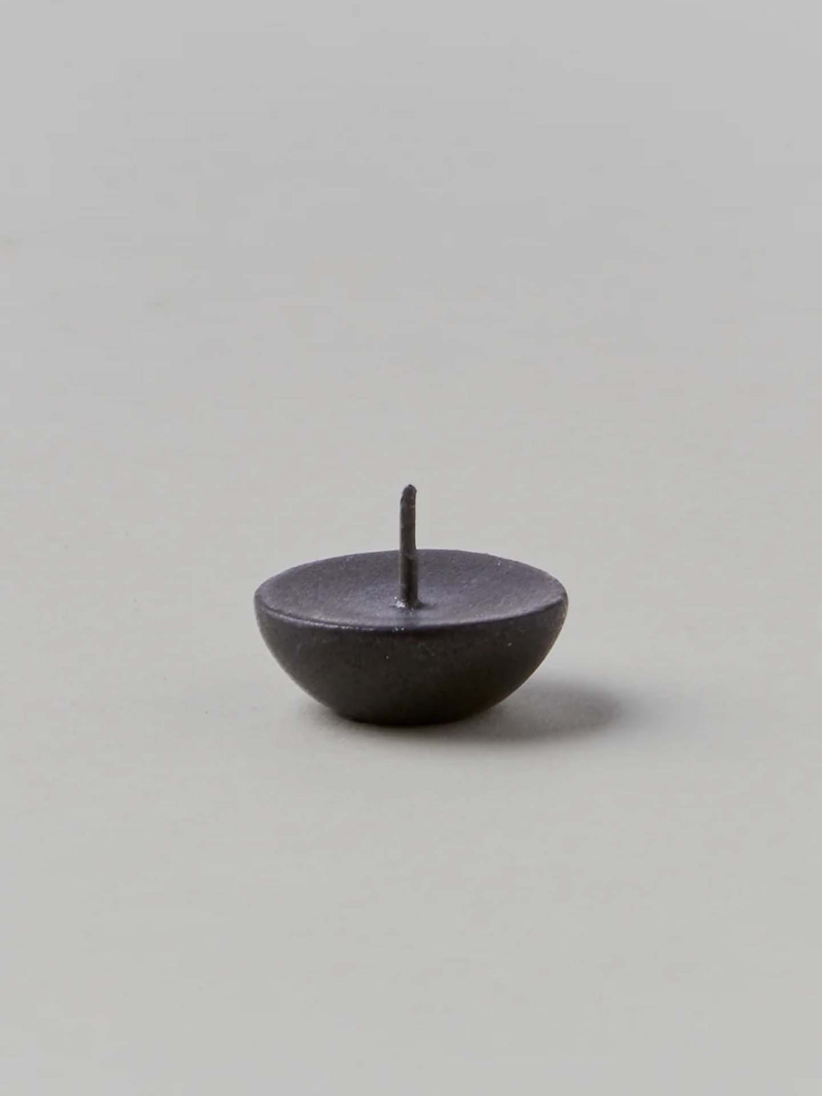 A small, dark metal pin with a round base and a sharp point facing upward on a neutral background mirrors the exquisite attention to detail found in Daiyo&#39;s Ceramic Candle Holder Circle – Black.