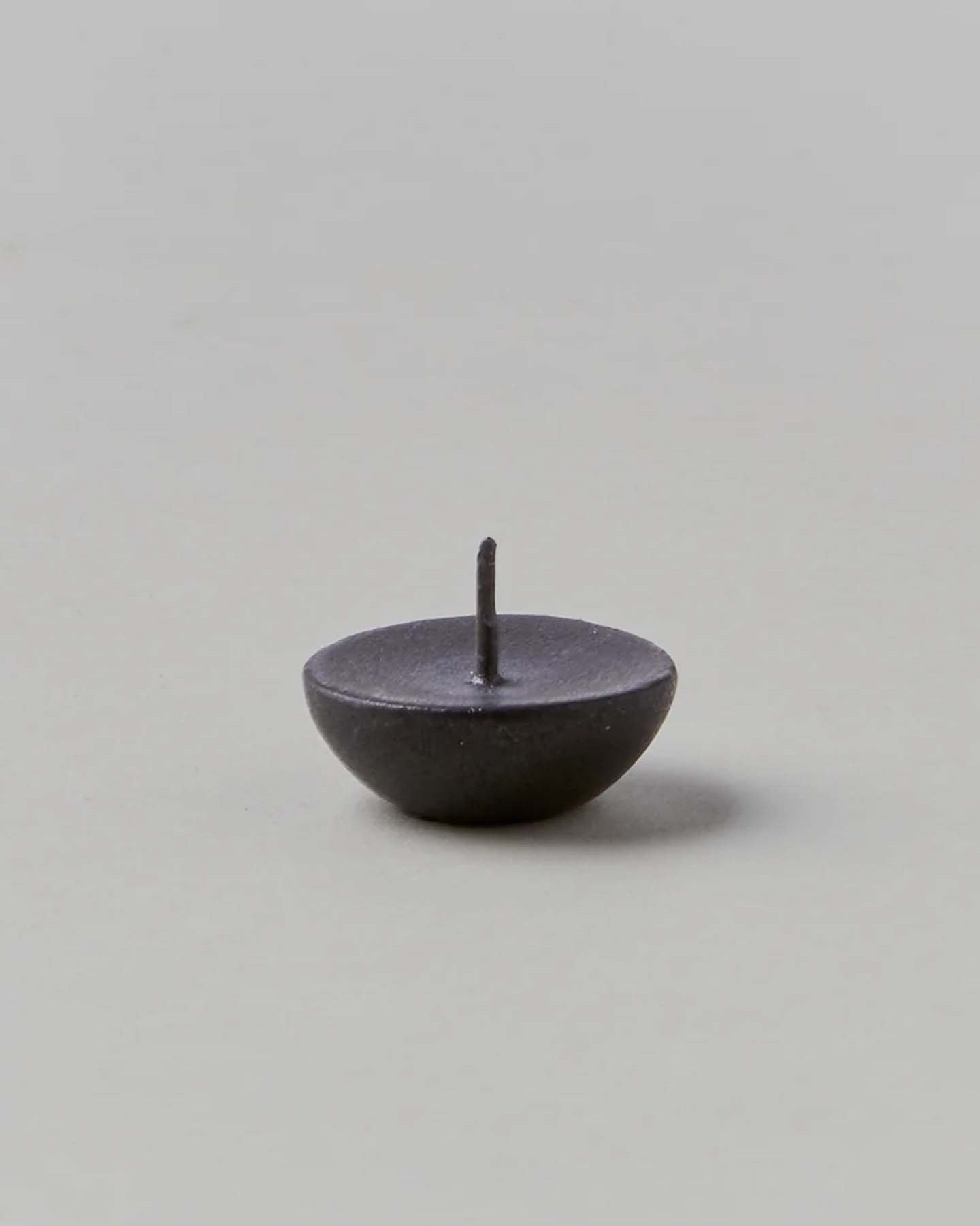 A small, dark metal pin with a round base and a sharp point facing upward on a neutral background mirrors the exquisite attention to detail found in Daiyo's Ceramic Candle Holder Circle – Black.