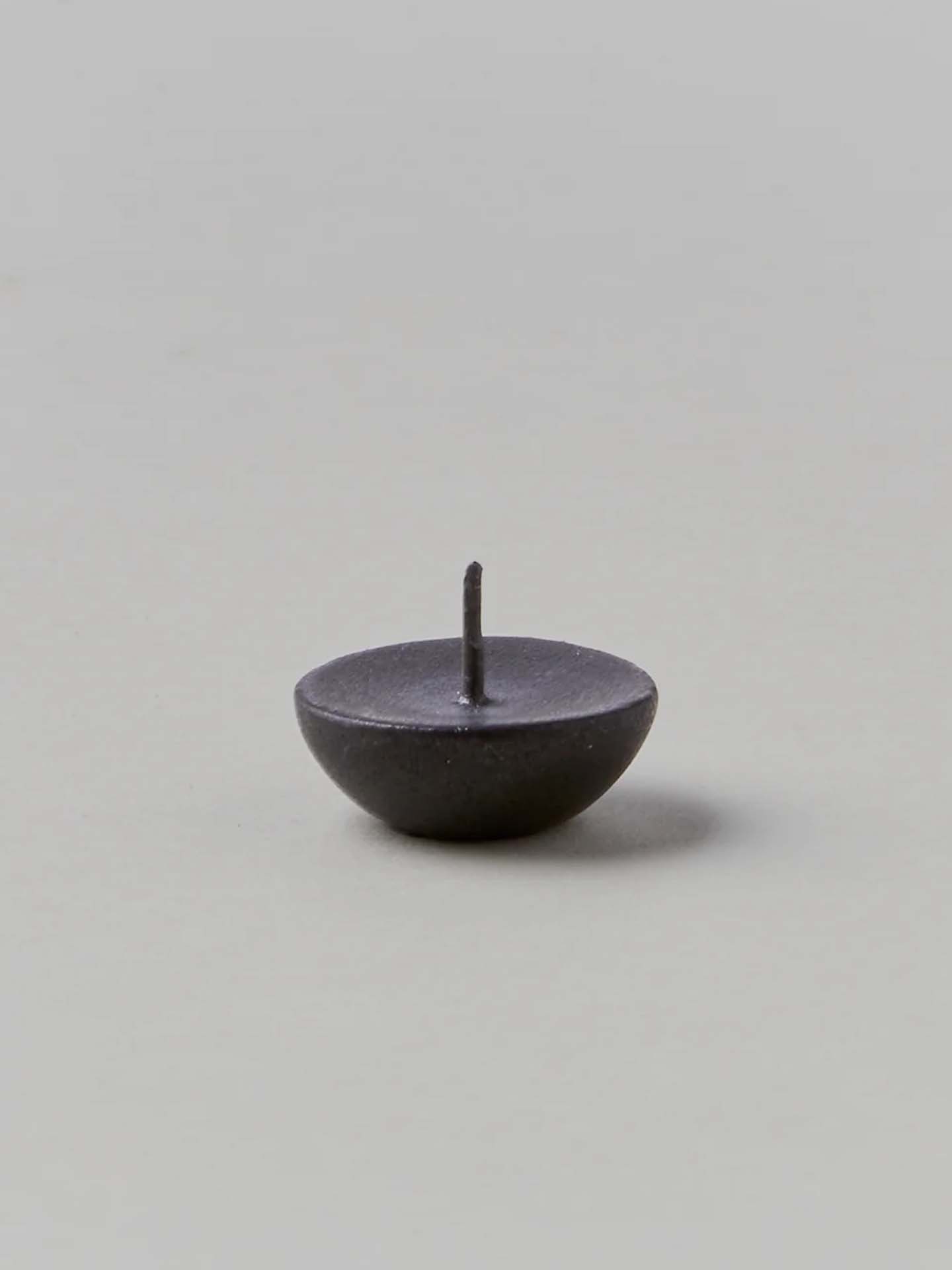 A small, dark metal pin with a round base and a sharp point facing upward on a neutral background mirrors the exquisite attention to detail found in Daiyo's Ceramic Candle Holder Circle – Black.