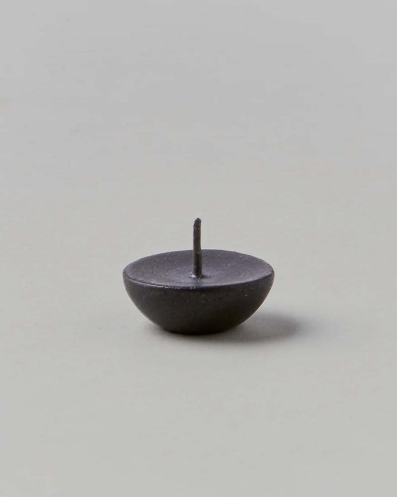A small, dark metal pin with a round base and a sharp point facing upward on a neutral background mirrors the exquisite attention to detail found in Daiyo's Ceramic Candle Holder Circle – Black.