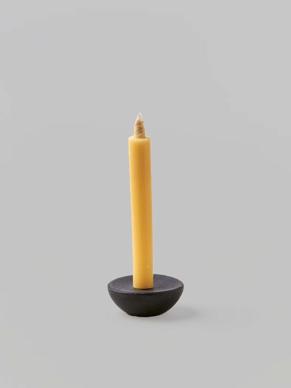 A single yellow Takazawa Candle is placed in a small, round Ceramic Candle Holder Circle – Black by Daiyo against a plain gray background, reminiscent of the intricate designs found in Shiga prefecture&#39;s miniature ceramic candle holders.