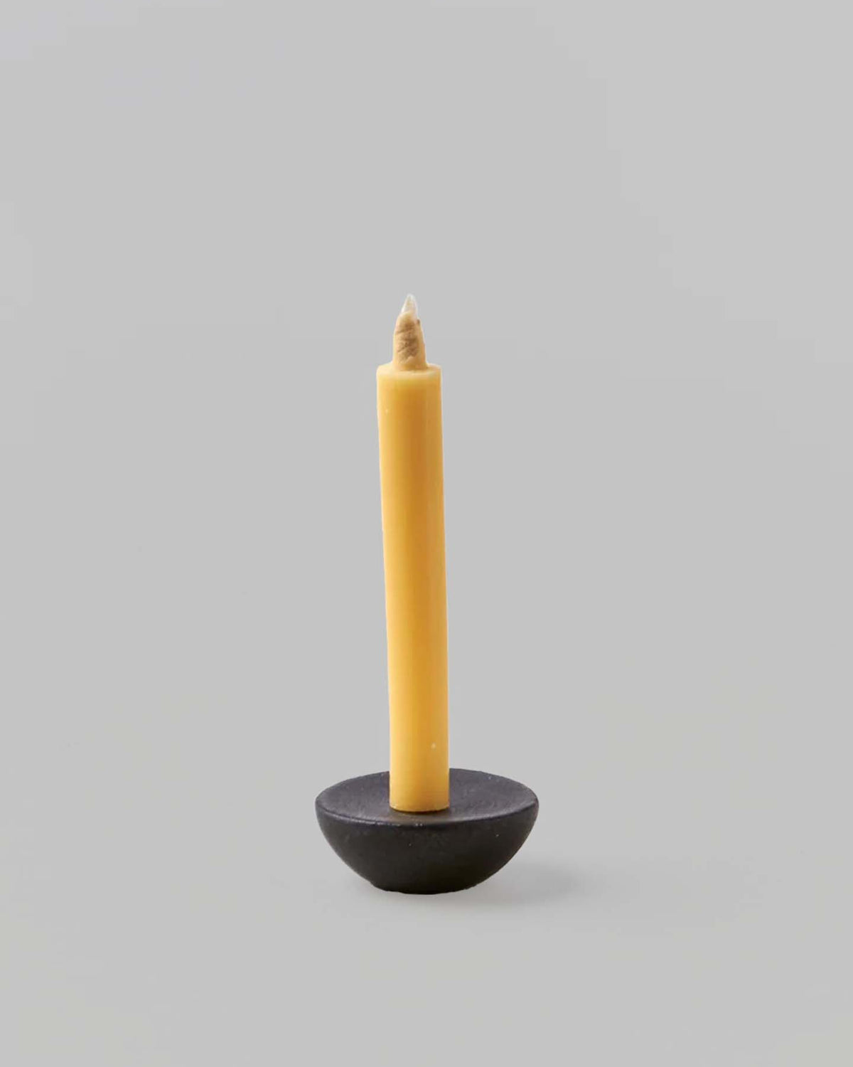 A single yellow Takazawa Candle is placed in a small, round Ceramic Candle Holder Circle – Black by Daiyo against a plain gray background, reminiscent of the intricate designs found in Shiga prefecture's miniature ceramic candle holders.