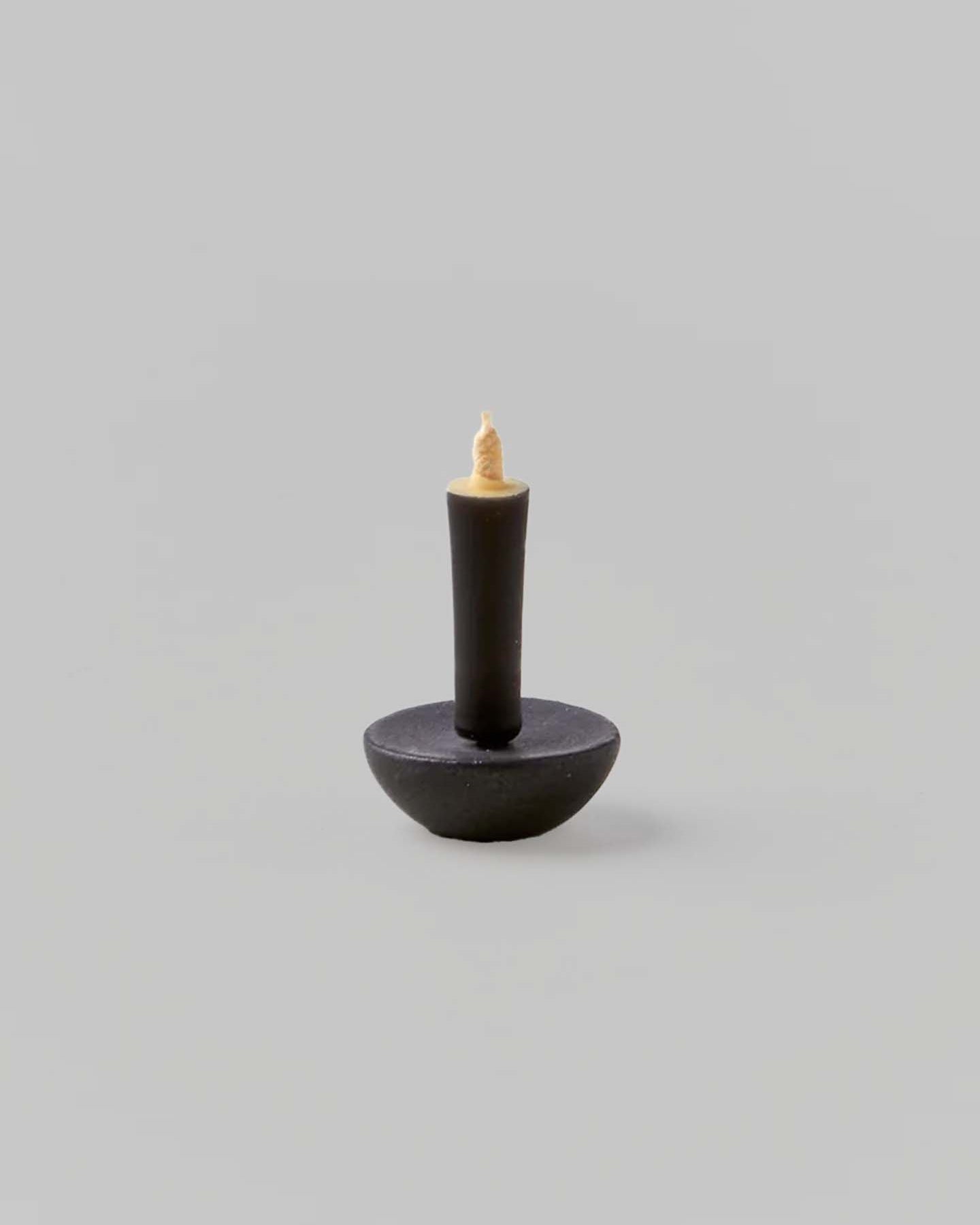 A small, dark metal pin with a round base and a sharp point facing upward on a neutral background mirrors the exquisite attention to detail found in Daiyo's Ceramic Candle Holder Circle – Black.