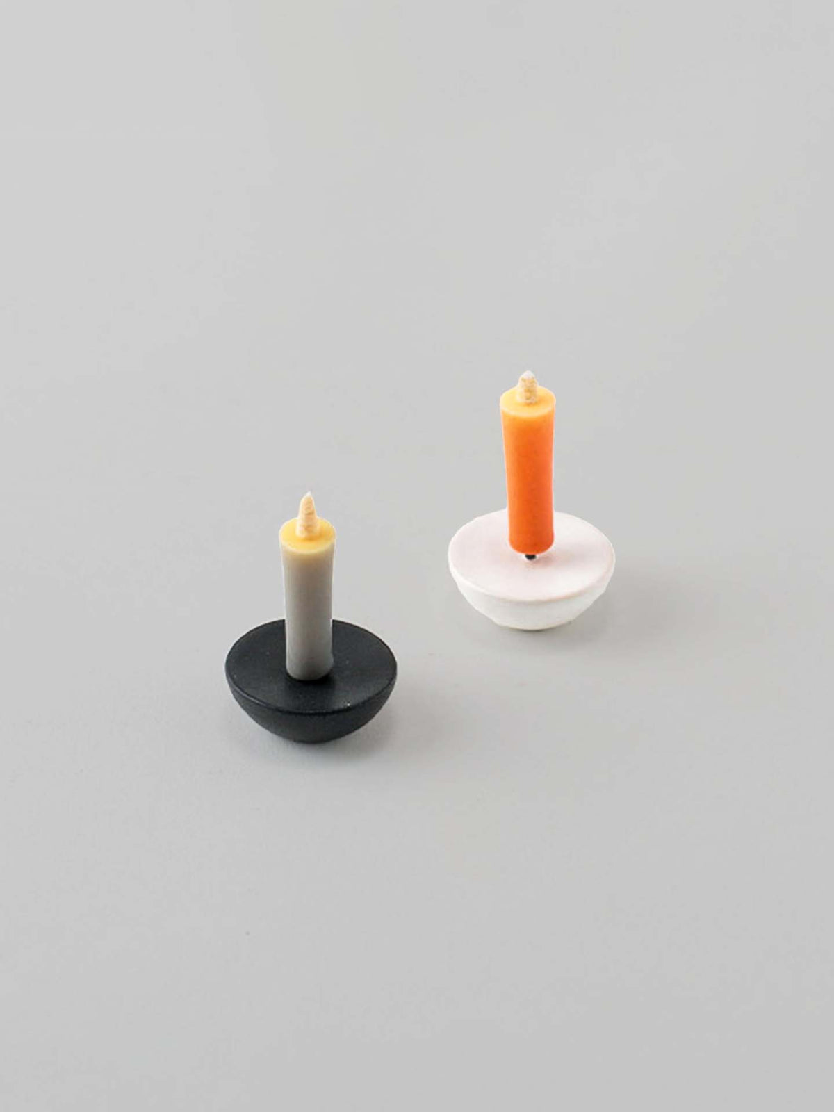 A pair of small rice wax candles, thoughtfully crafted by Daiyo artisans, featuring one with a ceramic circle holder in gray and beige, and the other with a ceramic circle holder in white and orange, placed on a soft gray surface. Ideal for elevating your meditation space.