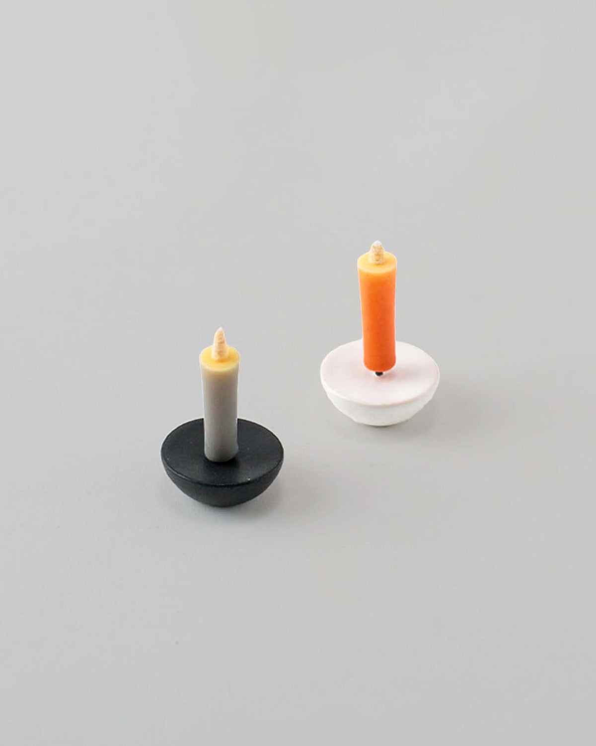 A pair of small rice wax candles, thoughtfully crafted by Daiyo artisans, featuring one with a ceramic circle holder in gray and beige, and the other with a ceramic circle holder in white and orange, placed on a soft gray surface. Ideal for elevating your meditation space.