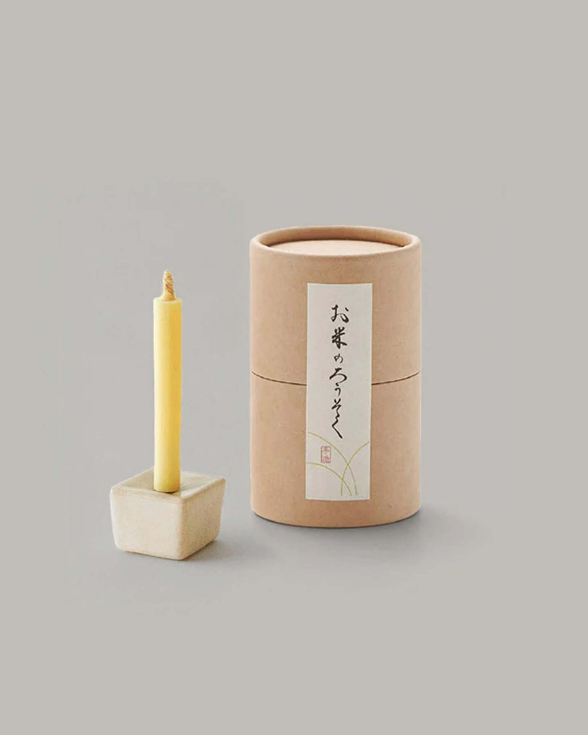 A tall and slender candle made from rice wax is beautifully displayed on an elegant iron and ceramic stand, accompanied by a cylindrical cardboard box adorned with Japanese writing. This stylish arrangement is part of the sophisticated Rice Wax Candle & Iron Stand 20pc Box Set – Black ⋄ White ⋄ Beige by Daiyo, making it perfect for any occasion.