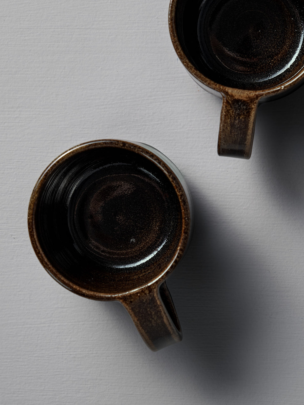 Two empty Studio Foon Everyday Stacker Cups – Large (300ml each) in Burnt Umber, viewed from above on a light grey textured surface.