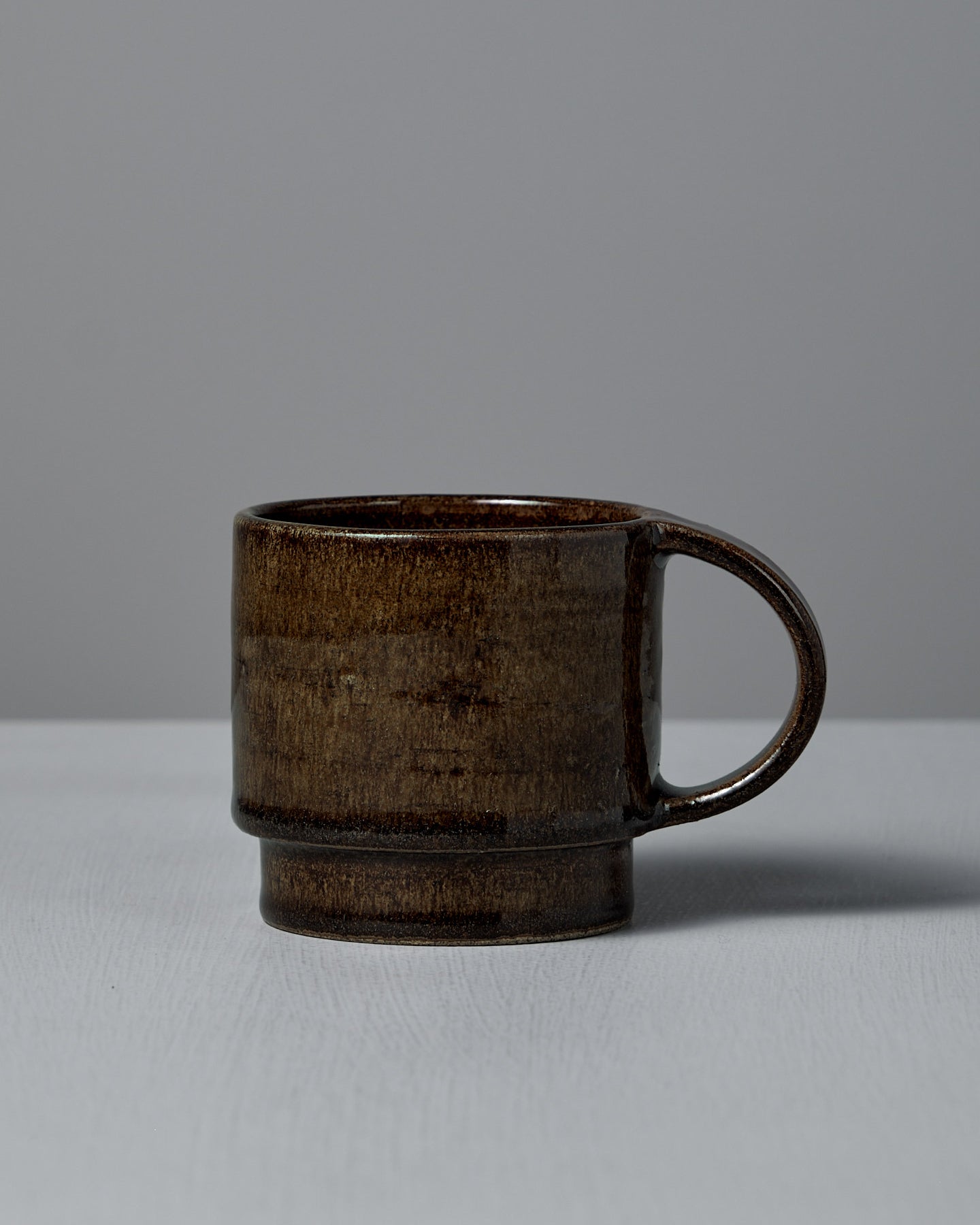 The Studio Foon Everyday Stacker Cup – Large in Burnt Umber, a handcrafted 300ml cup with a rounded handle, sits on a light gray surface against a plain gray background.