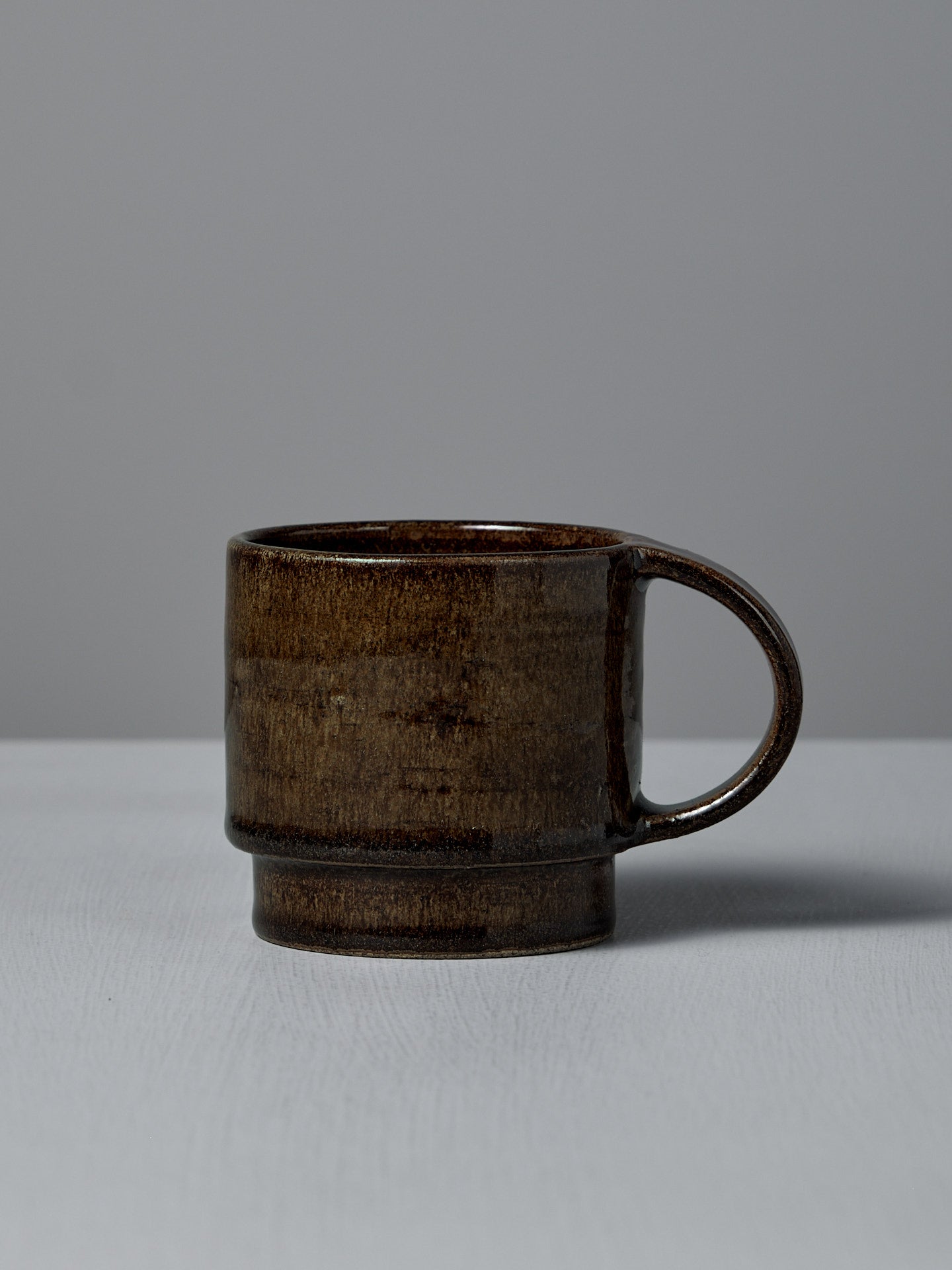 The Studio Foon Everyday Stacker Cup – Large in Burnt Umber, a handcrafted 300ml cup with a rounded handle, sits on a light gray surface against a plain gray background.